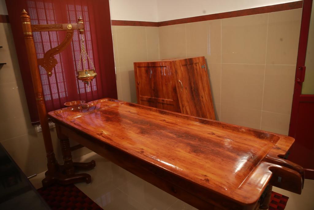 Traditional wooden Panchakarma treatment table with a brass oil lamp at Ayurdeva Irinjalakuda